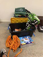 View of black container with Airhead green/black raft, life jackets, orange pulling rope, and box for inflatable swan pool float.