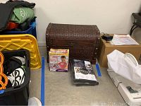 Full view of wicker trunk with Wonder Arms exercise kit box and Bark & Bar pet seat cover on floor next to it