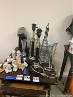 Photo of two black and brass metal lamps, several clear glass vases and pitchers, a metal banana holder, a popcorn machine with floral decoration, and multiple small ceramic figurines of children and animals arranged on a table.