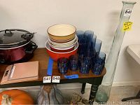 Photo showing 12 blue plastic glasses, 6 serving bowls stacked in a nest, and a tall clear glass vase on a wooden table.