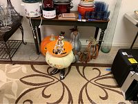 Overall view of Halloween pumpkin decor items including white pumpkin stand with skeleton figure and large orange plastic pumpkin.