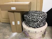 Two zebra print round hat boxes and two floral round hat boxes stacked together with cardboard boxes in background