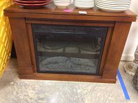 Front view of the electric fireplace showing wooden mantel, glass front, and simulated log fire inside.