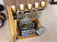 Photo of wall candle holder with five flameless candles on metal plates, 'HOME' clock sign, wicker basket with plaques and clock, wooden folding stand.