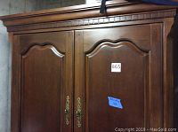 Front view of the entertainment cabinet showing double doors with decorative brass handles and carved wood details.