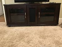 Front view of dark wood TV cabinet with glass panel doors and silver handles on carpet.