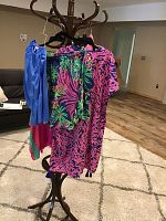 Three hangers with Lilly Pulitzer swimwear and shirts showing bright tropical prints and colors hanging on a coat rack.