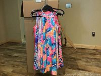 Four brightly patterned shift dresses hung on hangers in front of cardboard box