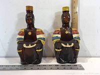 Front view of two Angostura Old Oak Rum Limbo Drummer ceramic bottles side by side with measurement rulers showing height and width.