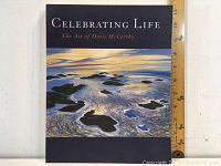 Front cover of the hardcover book "Celebrating Life: The Art of Doris McCarthy" showing a coastal scene painting with rocks and water. A measuring ruler indicates approx 11 inches tall.