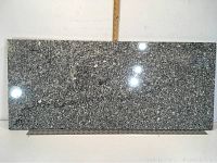 Front view of dark gray and white speckled polished marble slab, flat rectangle shape, placed against white background with ruler for size reference