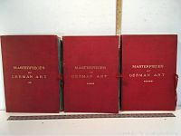 Three very large volumes with red covers titled 'Masterpieces of German Art.' The volumes are tied shut, standing upright side-by-side.