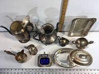 Photo showing assortment of silver plated and metal items arranged on a white surface with a ruler for scale.