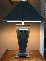 Side view of the lamp powered on, showing the textured trapezoidal base and black lampshade.