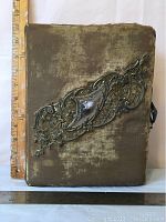 Front view of velvet album cover showing ornate metal decoration and ruler for scale
