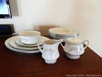 Photo showing stack of serving platters/plates, along with sugar bowl and creamer in Noritake Summerfield pattern on wood surface.