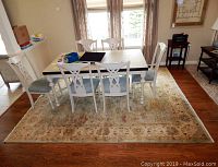 Full view of rectangular area rug under dining table with six white chairs with blue cushions in dining room setting.