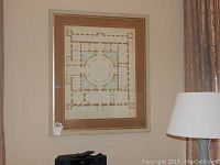 Framed architectural print photographed on a wall next to a lamp and electronic device.