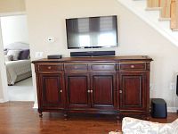 Front view of dark wooden buffet against wall with mounted TV above. Showing four drawers on top and three cabinet doors below.