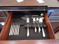 Drawer with knives on left side and various serving flatware pieces including pie server, ladle, forks and spoons on right side.