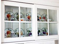 Photo showing dessert plates, cups, and saucers with vibrant fruit designs displayed inside a white cabinet.
