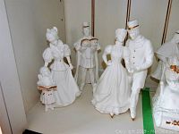 Front view of Lenox bisque porcelain figurines including woman and child carolers, man caroler, and skating couple music boxes on shelf.