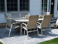 Beige aluminum dining table surrounded by six matching chairs on a stone paver patio