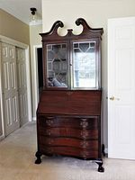 Front view of dark wood antique secretary desk closed, showing glass cabinet doors, scroll-top and claw feet.