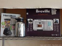 Hamilton Beach smoothie blender box, Breville Custom Loaf bread maker box, and Trudeau hot liquid carafe placed on metal shelf.
