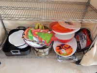 Whole lot showing casserole dishes, roasting pans, plastic food storage containers, holiday-themed paper plates, melamine platters, and other cooking accessories on metal shelf rack