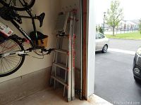 Aluminum Little Giant Ladder System Type 1A, industrial grade, with orange locking mechanisms, leaning inside garage near bicycles and garage door track.