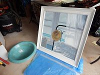 Photo showing the framed painting and turquoise ceramic bowl placed on blue padding in a garage setting.