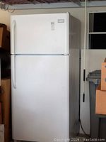 Full view of the white Frigidaire top freezer refrigerator from an angle, showing the front and side with visible handles and product label.