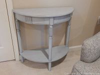 Front view of distressed gray demilune accent table showcasing shape, legs, and lower shelf.