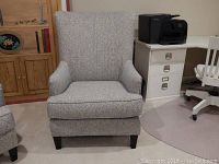Front view of the gray paisley upholstered wing chair with dark wooden legs and cushioned seat.