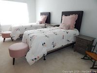 Twin beds with floral quilts, pillows and round pink velvet hassock.