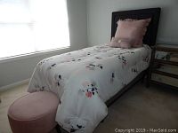 Twin bed with floral quilt, pillowcase, pillows, and pink velvet round hassock