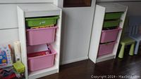 Photo showing two white melamine shelving units side by side, each with three plastic bins (top green, two pink).