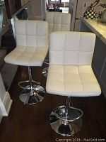 Three white vinyl and chrome bar stools grouped at counter edge