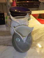 Two owl vases seen from front and angled showing ceramic owl vase gray/white and glass owl vase purple with gold trim on bowls
