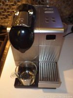Front view of the Nespresso coffee machine on countertop with glass cup on tray
