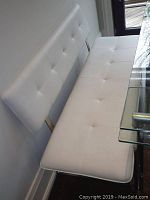Front view of white vinyl tufted bench against wall next to glass-top table
