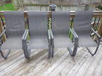 Photo of four outdoor chairs with metal bases and gray vinyl mesh backs and seats, arranged on a wooden deck.