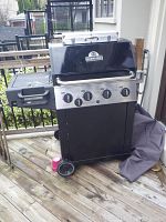Full view of the Sterling natural gas barbecue grill on a wooden deck, showing the grill body, control panel, side burner, and wheels.