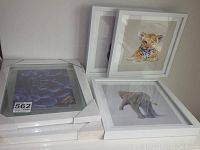 Two new white 11x14 picture frames stacked next to three framed prints featuring animal portraits.