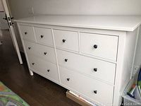 Front view showing all eight drawers with black knob handles on hardwood floor