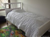 Side view of the white IKEA kids bed frame with bedding including a white comforter with blue stars and a colorful playmat underneath.