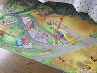 Photo of colorful children's play rug illustrating roads, buildings, and railroad tracks on wooden floor