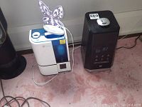 Two humidifiers side by side on carpet, one with butterfly night light attached, showing wear and dirt marks
