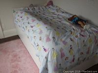 Full view of the IKEA kids bed set up with princess themed bedding and a doll on top.